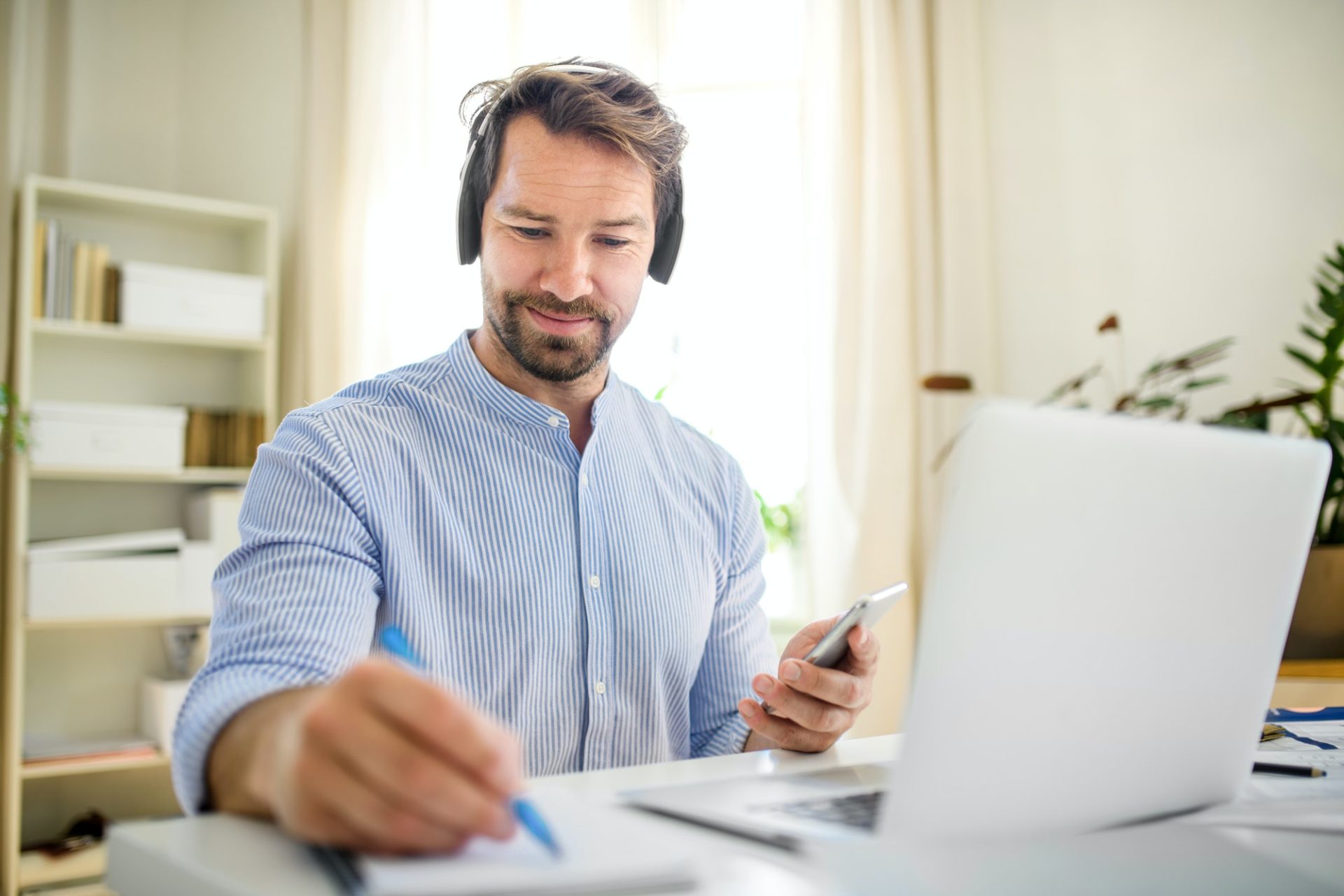 Mature businessman with headphones and laptop indoors in home office, working