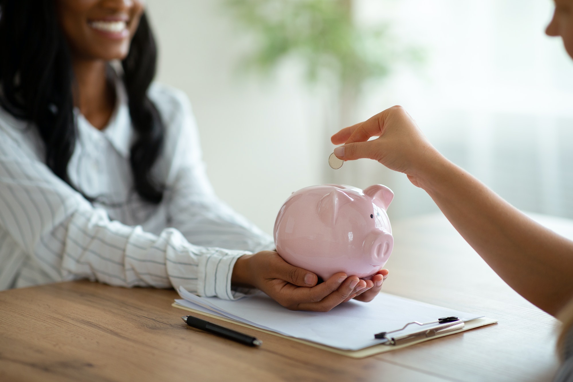 Financial planning concept. Closeup of business women putting coin into piggy bank at modern office